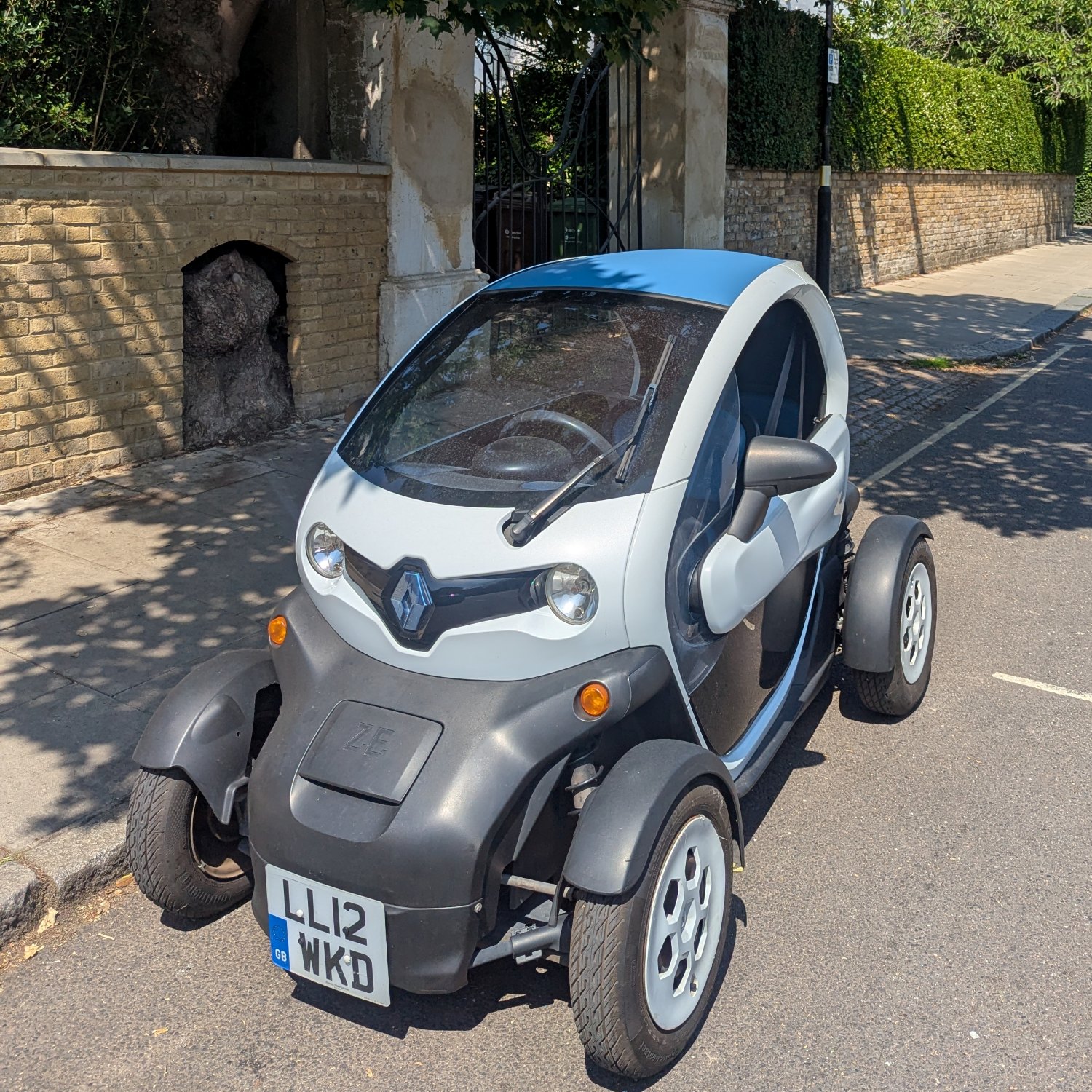 White 2012 Renault Twizy Colour with a blue roof, registration LL12 WKD, parked on a
              tree-lined London street in June 2026